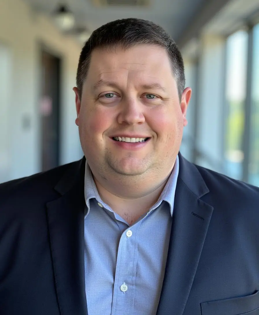 Smiling man in a blazer and collared shirt indoors.
